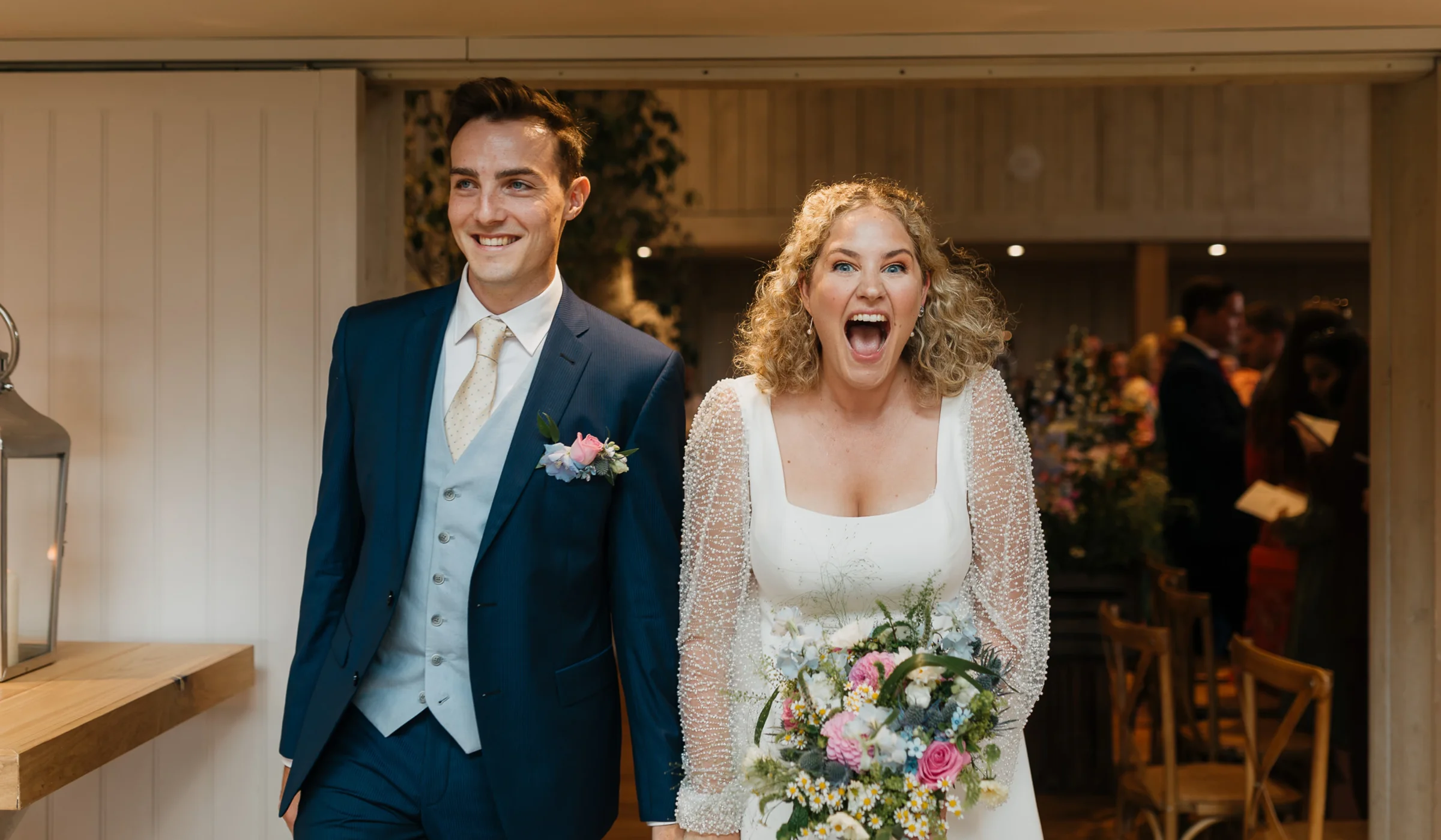 Bride and groom entering their barn reception, the bride in a satin wedding dress with sheer beaded sleeves