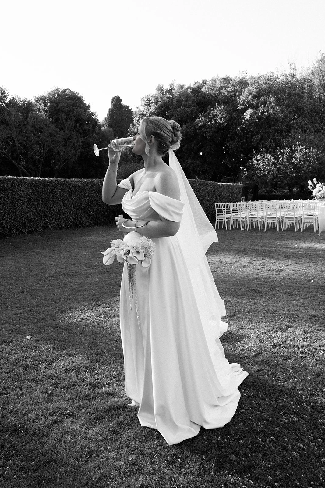 Custom wedding dress with draped satin bodice and full skirt, side view with her veil in the garden