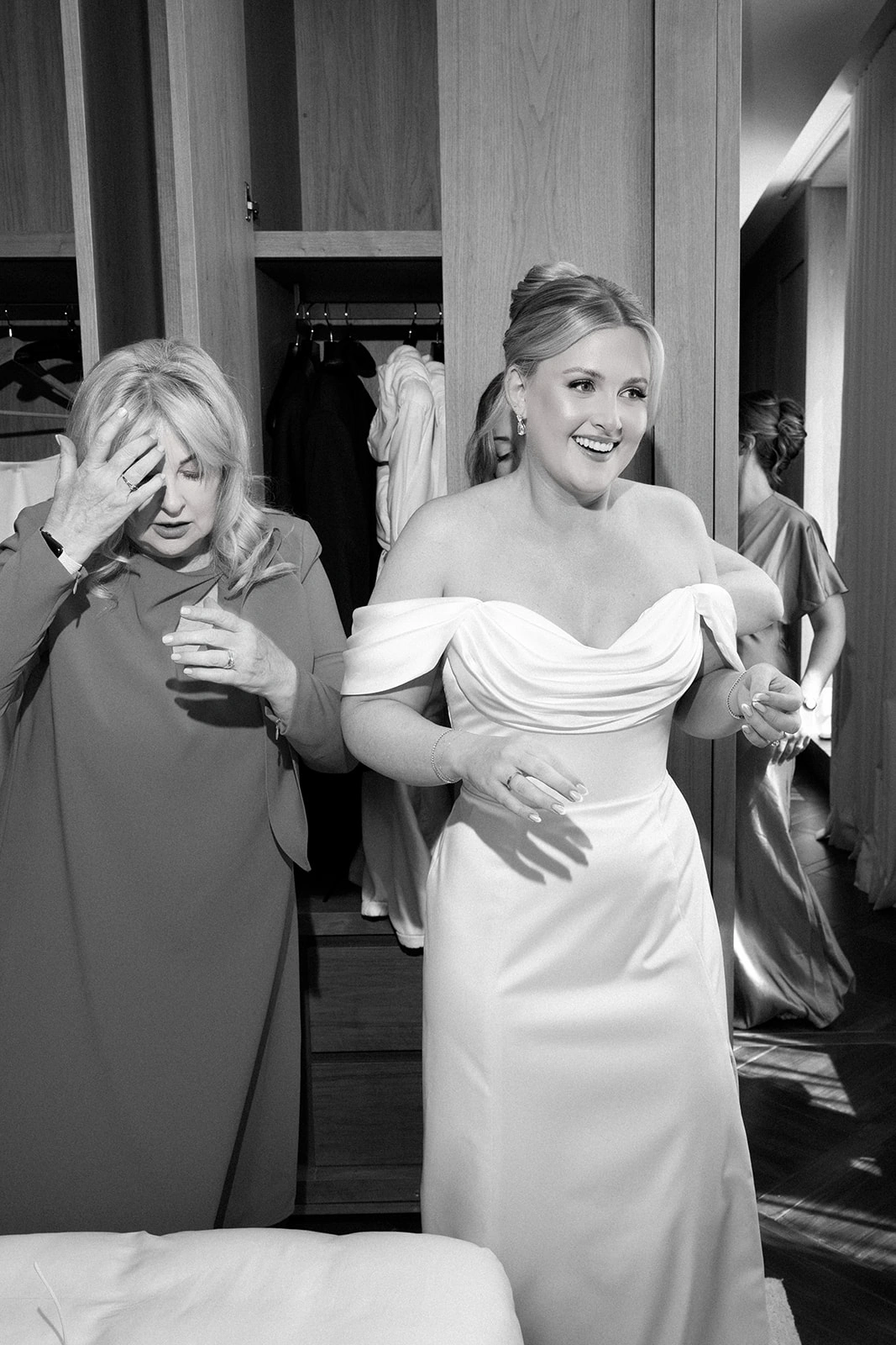 Custom wedding dress with a draped off-shoulder satin bodice, bride getting ready with her mother